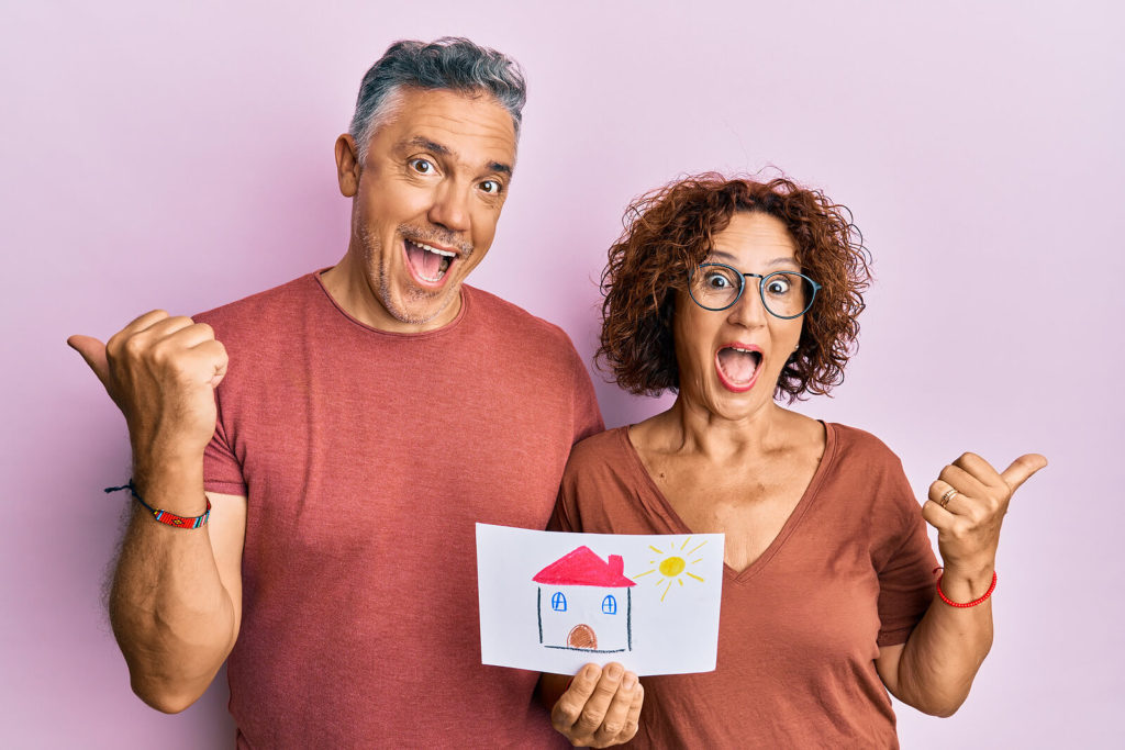 middle aged couple holding up a picture of a house.